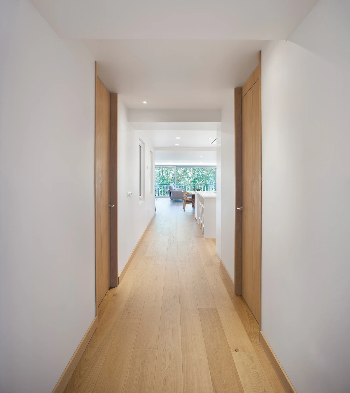 Pasillo ancho con puertas de madera de suelo a techo y continuidad hacia el salón en Ferrol. Diseño por SEA Arquitectos.